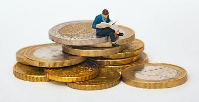 monedas de euro con muneco en miniatura de hombre leyendo libro